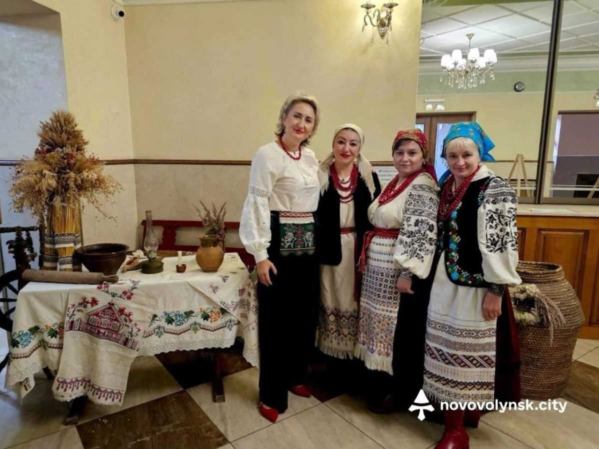 Чотири жінки в традиційних строях біля столу з рушниками та снопом